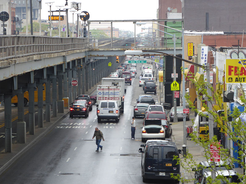 Bird’s eye view of a road with elevated train tracks on the left and stores on the right