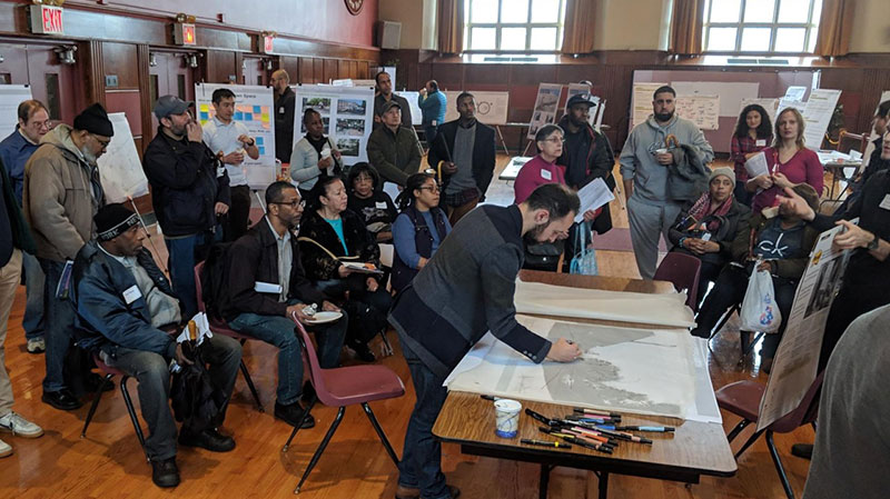 People seated and standing around a table with posters behind them.