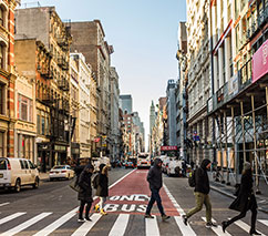 Streetscape with storefronts and people crossing a crosswalk.