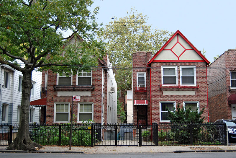 Two houses in front of a fence and sidewalk