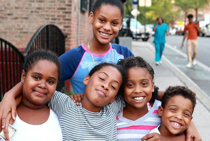 Five children hugging and posing for a photo on a sunny day