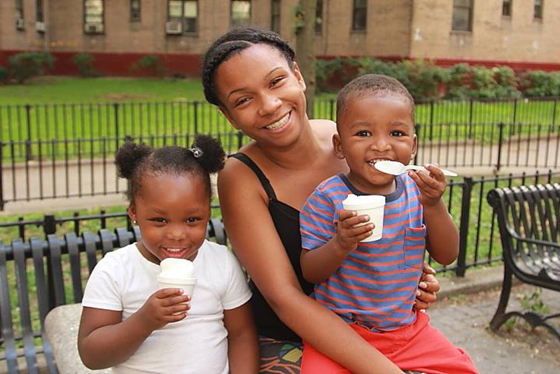 girl and two children sitting on bench in front of buildings eating ice cream