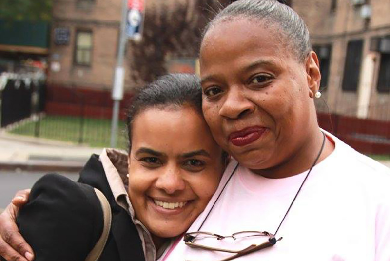 two women hugging and smiling for a photo in front of bus stop in the day