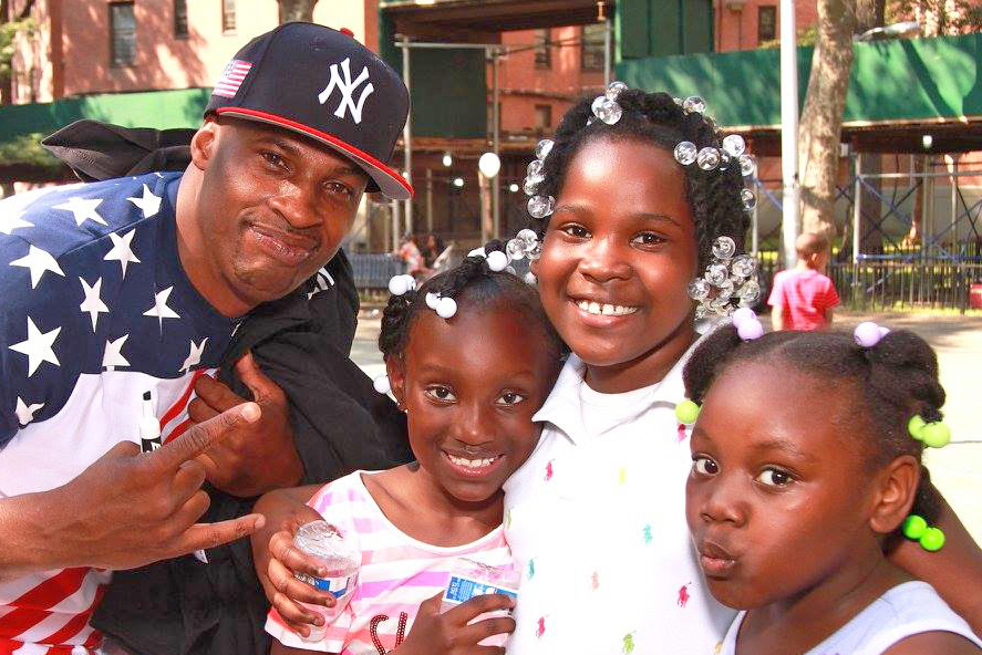 man with Yankees hat and three girls holding water bottles and smiling in front of building