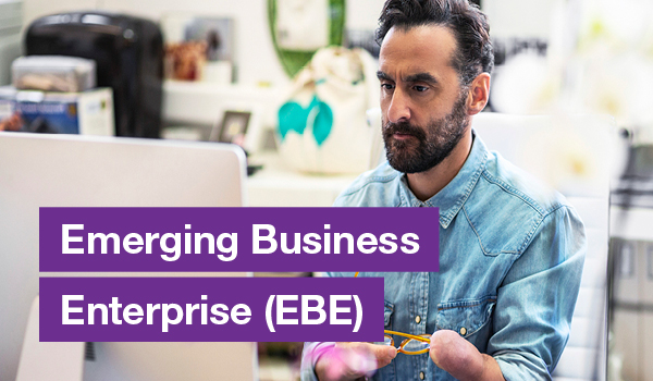 Man with limb difference using computer with text on the left that says Emerging Business Enterprise (EBE)