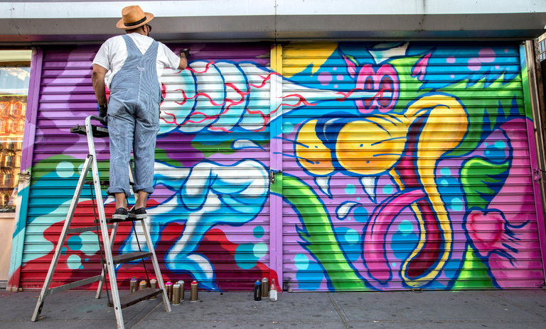 artist on ladder painting mural on pull-down security gate on Lower East Side