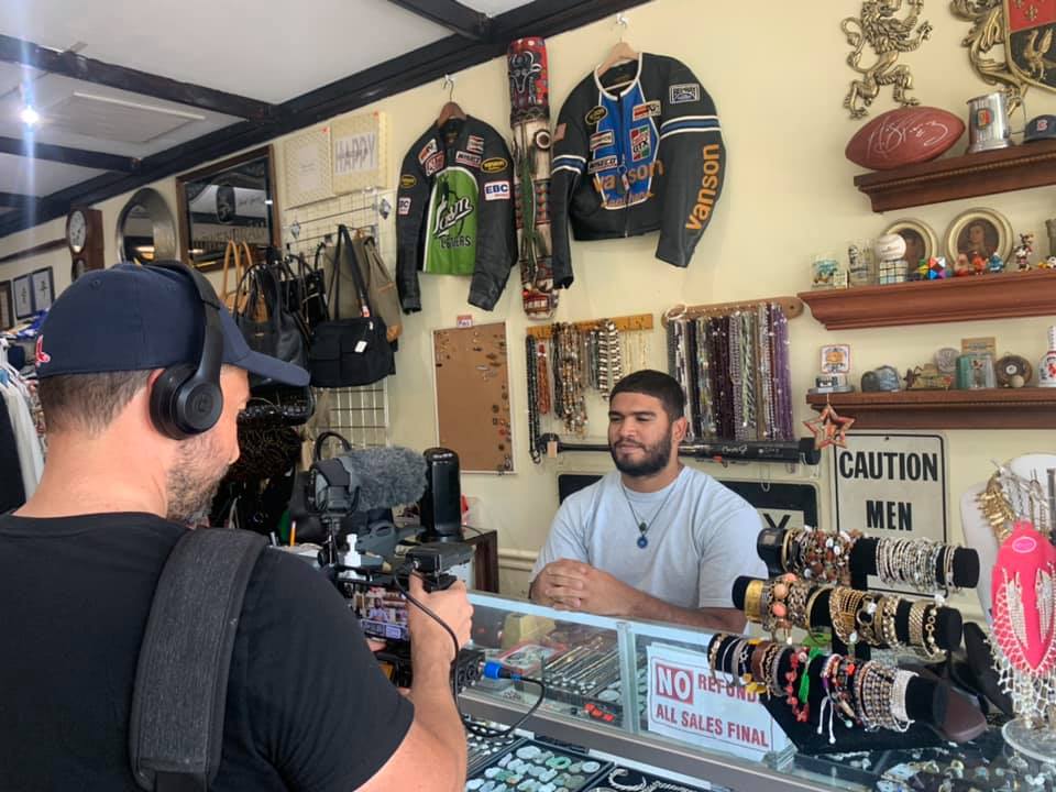 Man filming a video featuring a worker behind the counter of a small business thrift store