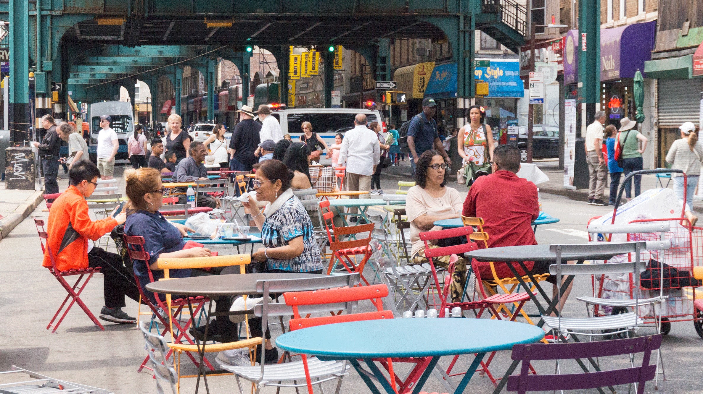street scene with people seated at community tables under an elevated train track