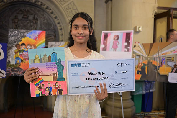 A girl smiles proudly with her artwork and prize check