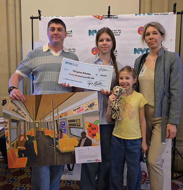 A girl of middle school age smiles while standing with her family holding her artwork
