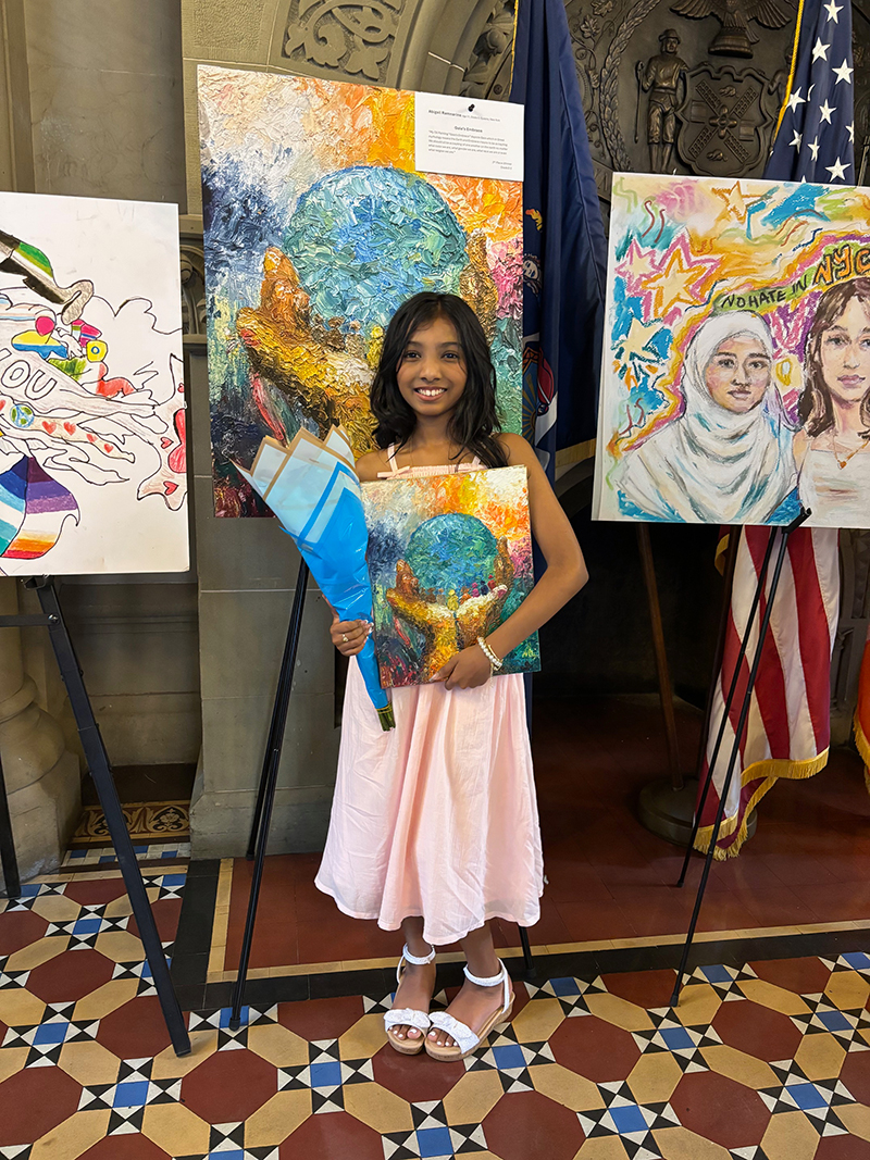 A girl of elementary school stands next to the artwork that won HeARTwork context