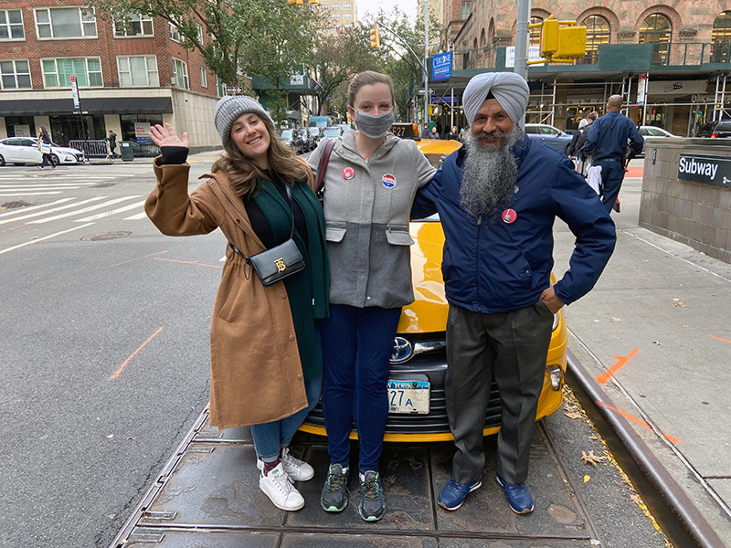 Two women and a man stand in the street in front of a taxi