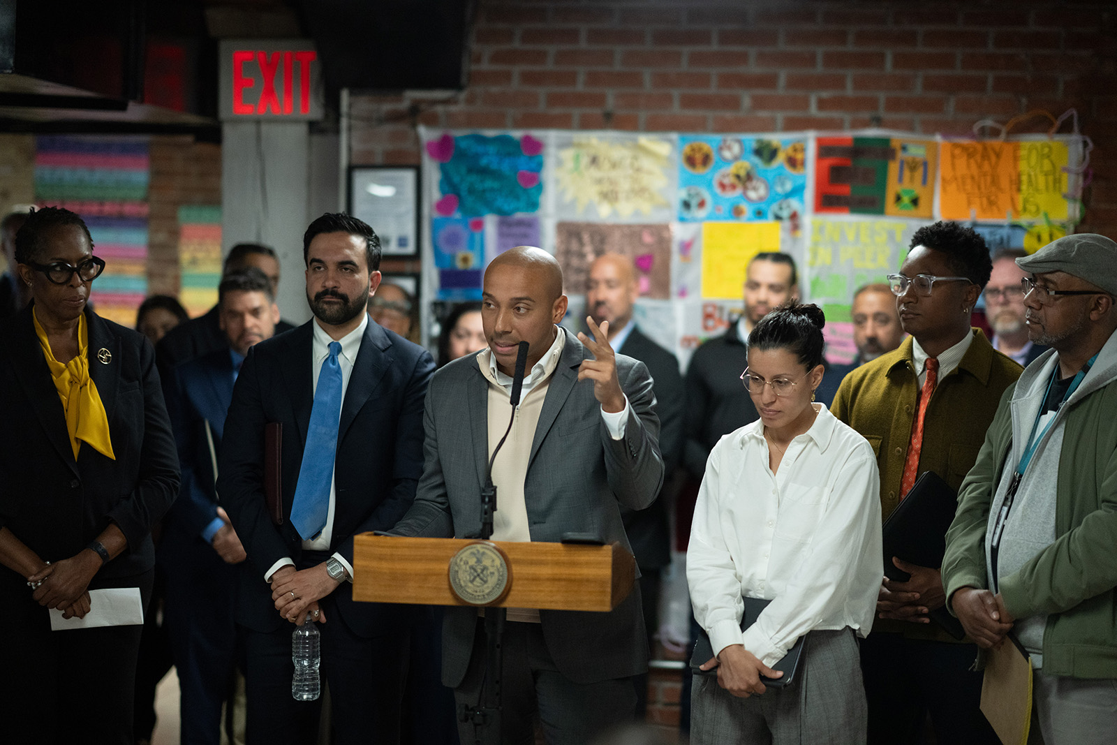 Mayor Mamdani and other people standing by a man at a podium