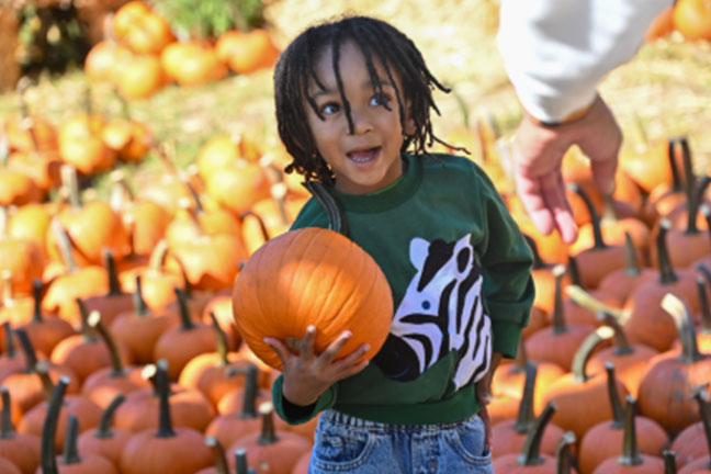 a kid holds a Halloween pumpkin with his right arm