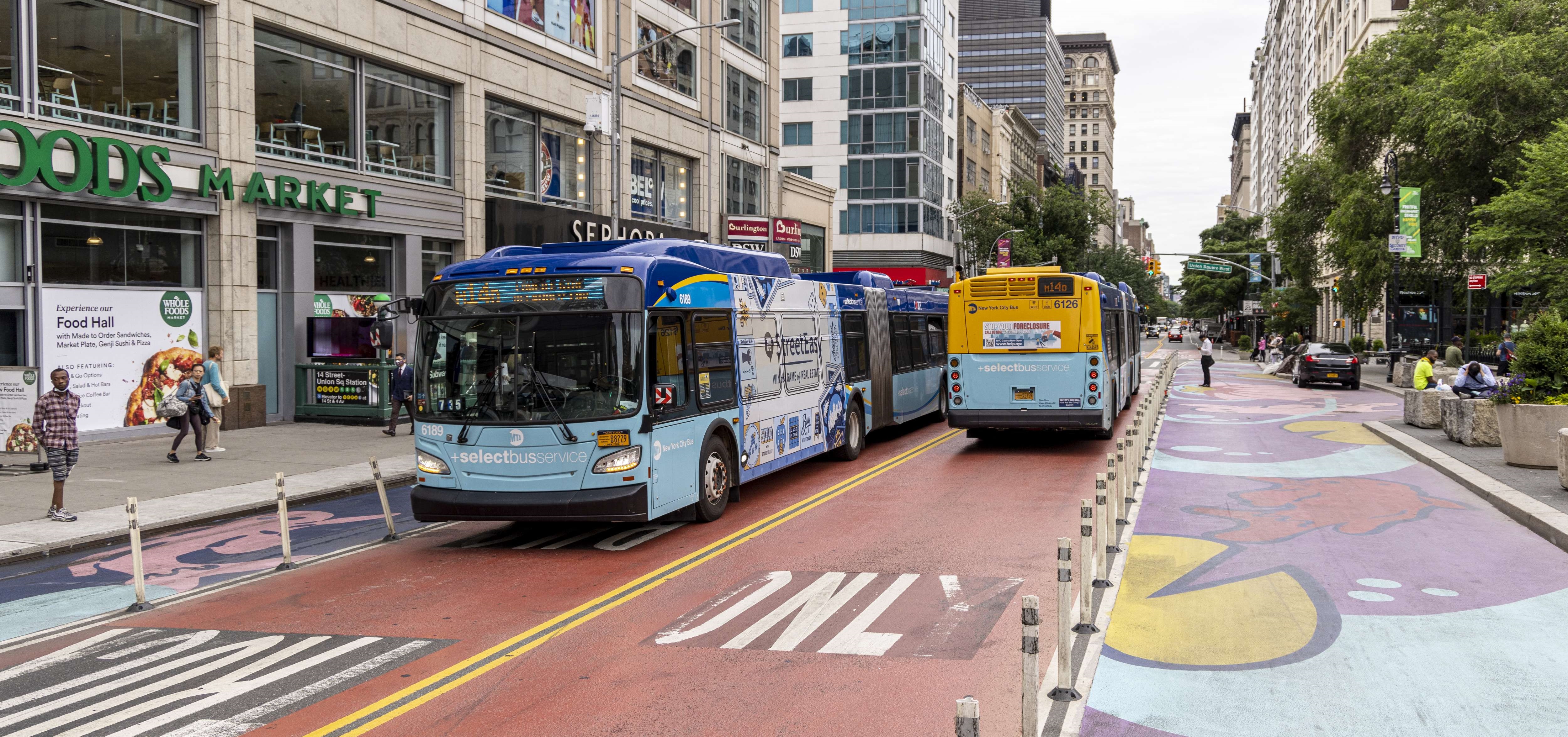 Two blue M T A buses drive along ride bus and truck only lanes along Manhattan's 14th Street car-free busway.