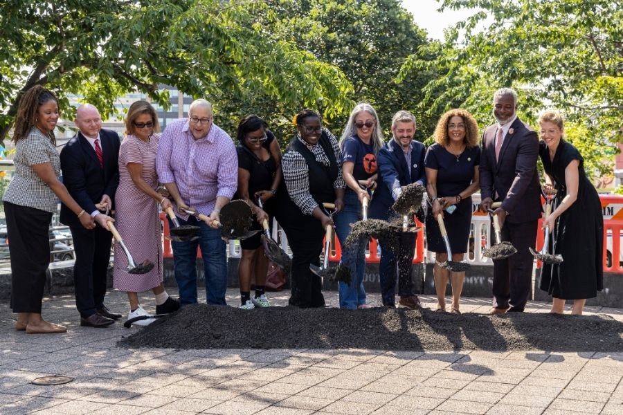 Alt text: A group of people shovel dirt to represent the start of construction of offset bus lanes along Fordham Road in The Bronx.]