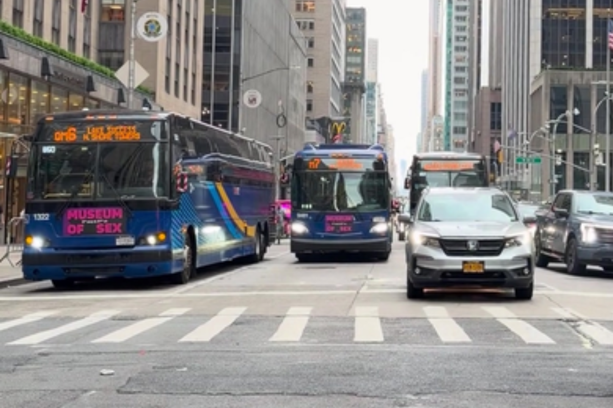 View of city buses and personal vehicles traveling on a wide avenue in Midtown Manhattan.