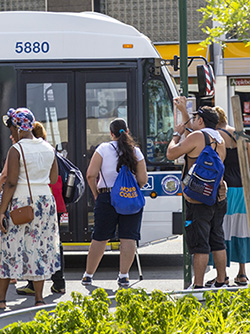 On a summer’s day people wait to board a bus on Tremont Avenue in the Bronx.