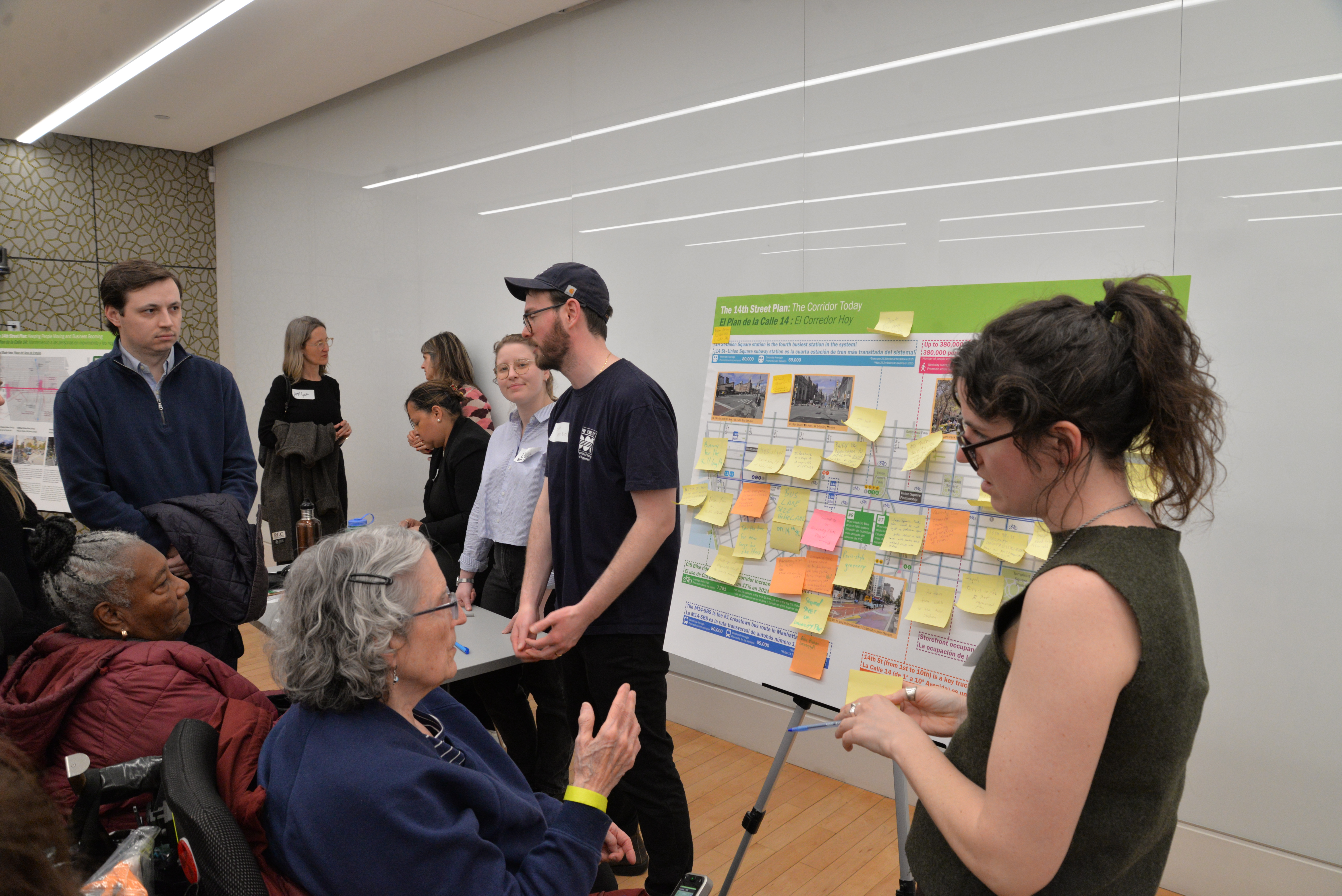Two older adults in mobility devices provide feedback to N Y C D O T representatives about 14th Street.