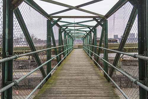 An empty pedestrian bridge with wooden planks and painted green steel beams on both sides and over the bridge