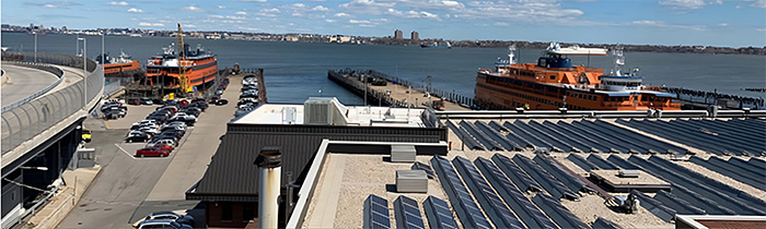 Three large orange ferries are docked at piers along the waterfront in Staten Island