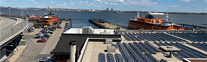 Three large orange ferries are docked at piers along the waterfront in Staten Island