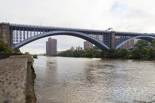A bridge with an arched bases crosses high over a river in New York City