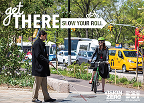 A pedestrian walks on a sidewalk using a white and red cane. A cyclist on a bicycle path stops ahead of the pedestrian crossing.