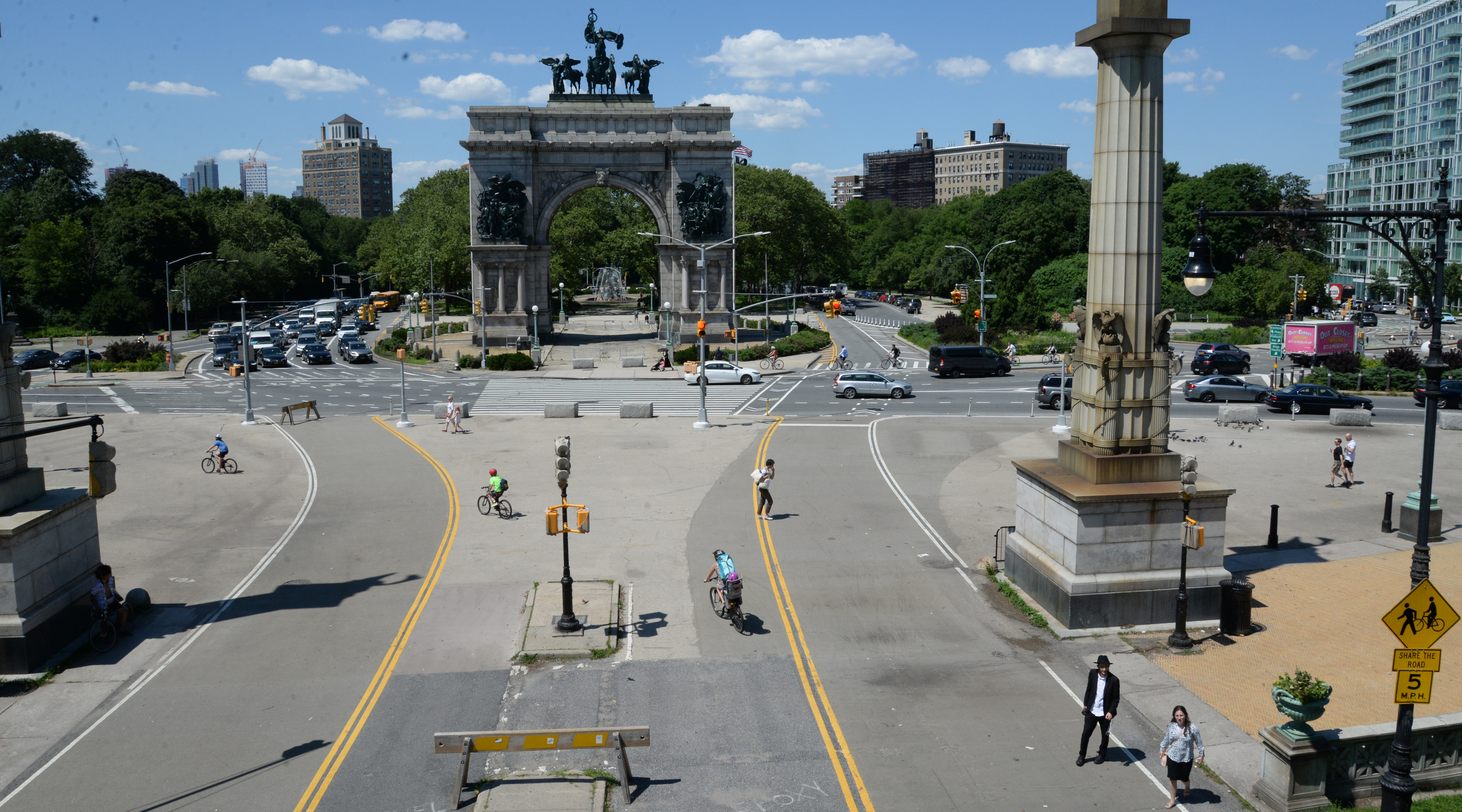 Two lanes of pedestrian and cyclist traffic go in and out of a park leading to a circle of vehicular traffic around the Soldiers' and Sailors' Arch in Grand Army Plaza.