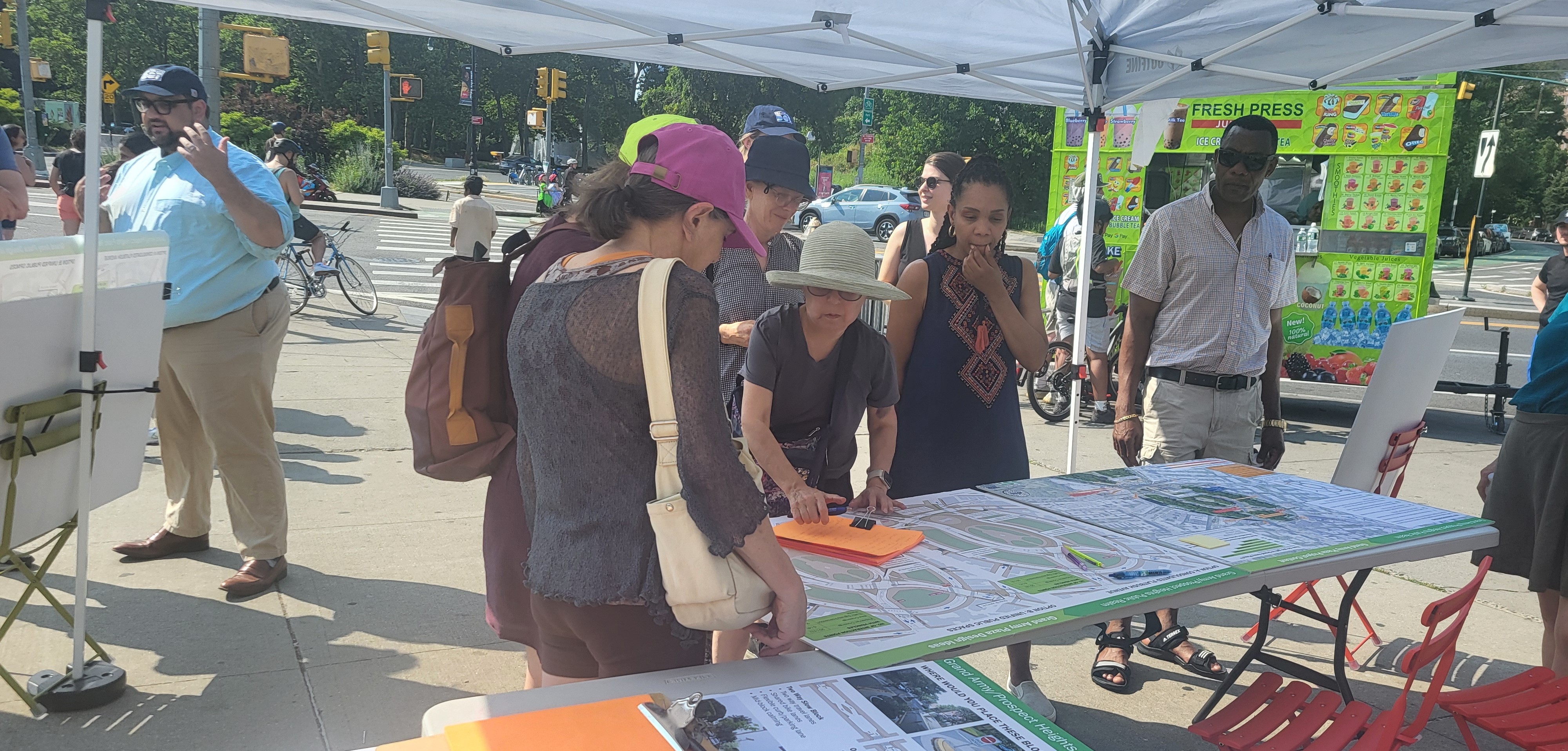 People talk at tables and informational boards at a public gathering outside