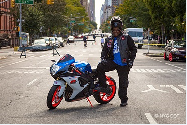 A person wearing motorcycle gearing including a helmet, stands beside a motorcycle parked on a street closed to traffic.