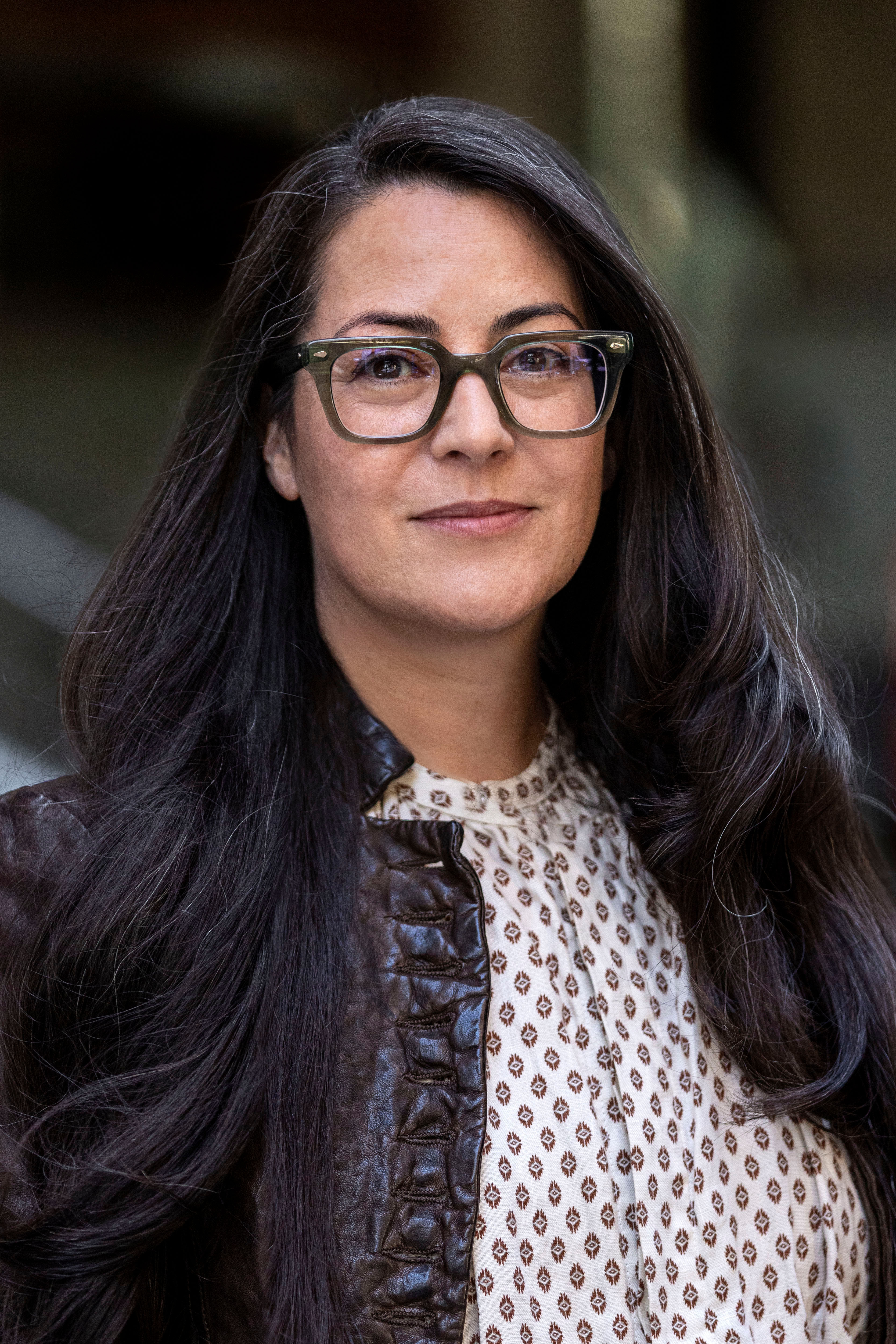 Portrait of New York City Department of Transportation's Queens Borough Commissioner Nicole Garcia with long dark hair, wearing glasses and a brown jacket over a patterned button down shirt.