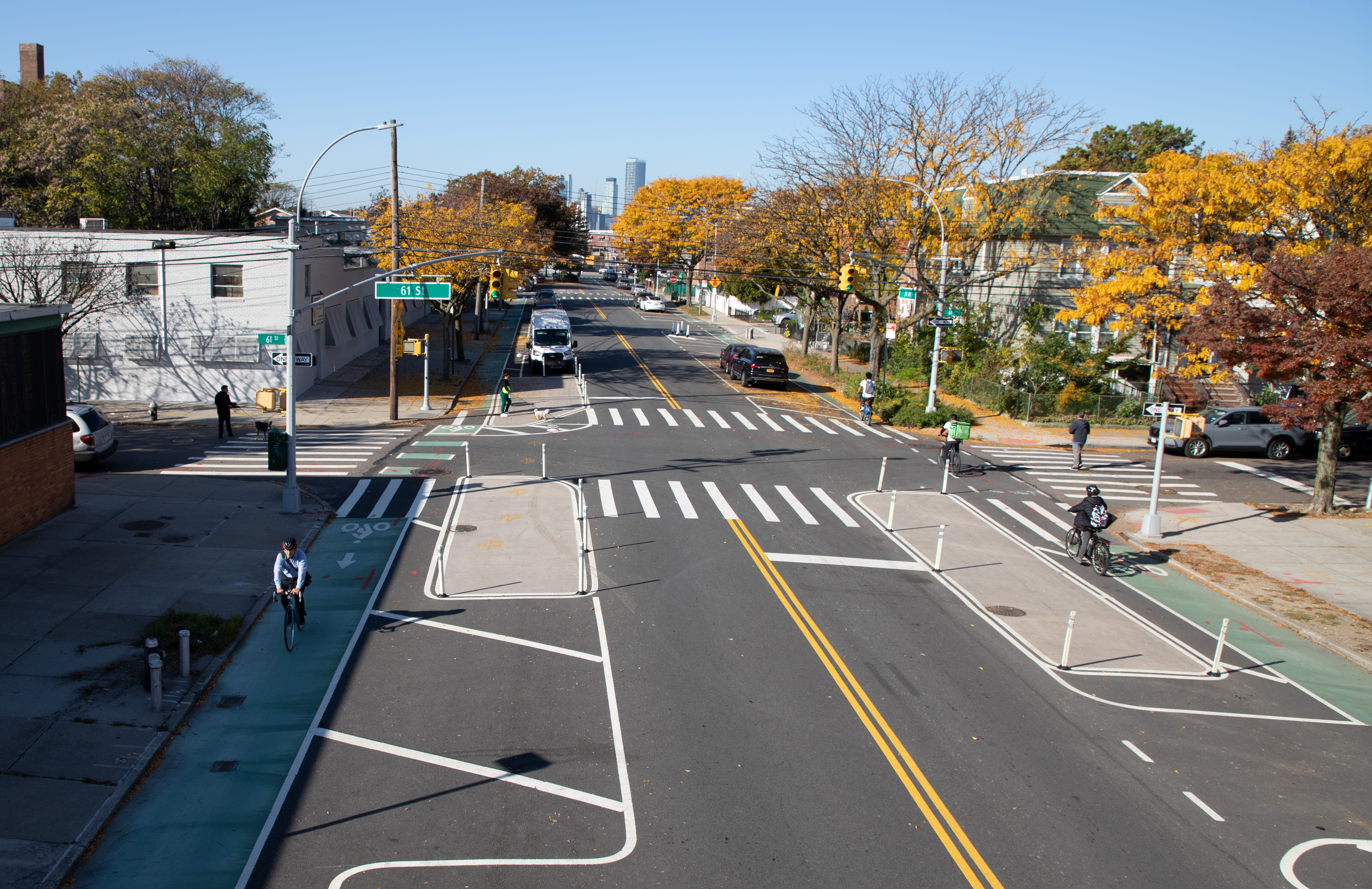 Multiple cyclists ride along a redesigned street in Queens featuring parking-protected bike lanes on each side.