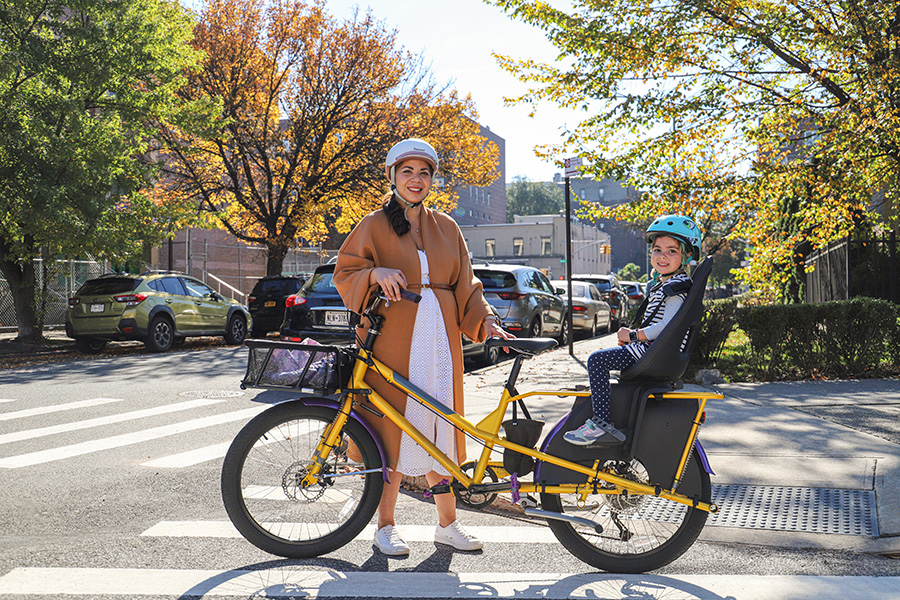 A woman stands next her bicycle, her son sits on a child seat in the back of the bike.