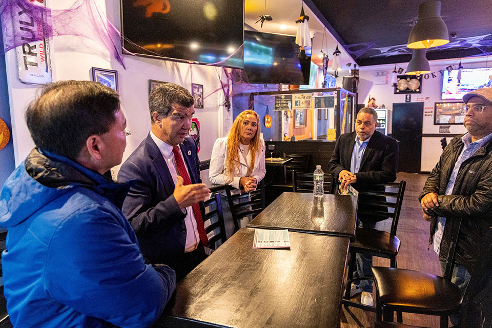 Commissioner Rodriguez and food establishment owners stand around a long table inside a restaurant in the Bronx.