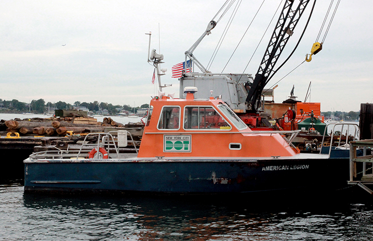 A small orange and navy blue motor boat with the NYC D O T logo and name American Legion, is docked.