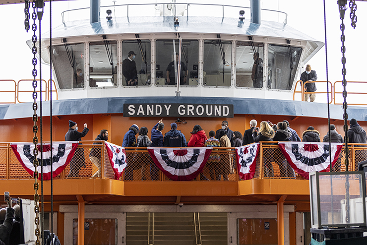 People gather on board an orange ferry named Sandy Ground.
