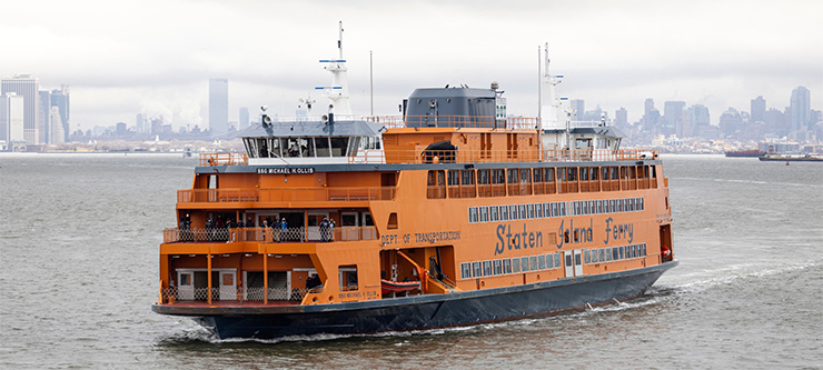 A large orange Staten Island Ferry travels in the New York Harbor on an overcast da