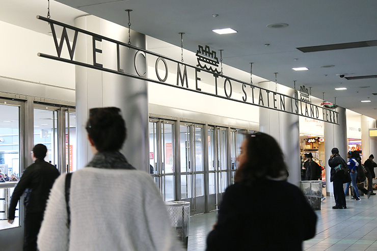 People walk inside the St. George Ferry terminal below a sign that reads “Welcome to Staten Island Ferry”