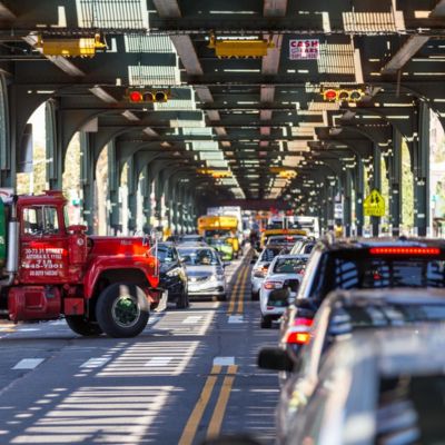 Heavy vehicular traffic and elevated train tracks along 31st Street in Queens.