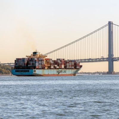 A large ship carrying shipping containers travels near the Verrazzano Narrows bridge. 