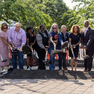 A group of people shovel dirt to represent the beginning of construction of off-set bus lanes along Fordham Road in The Bronx.