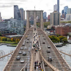 Cars, bikes, and pedestrians travel across the Brooklyn Bridge, between Manhattan and Brooklyn.