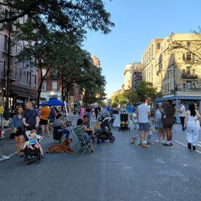People sit, walk, and stand together on a street temporarily closed to vehicular traffic and open for pedestrians.