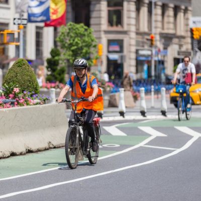 Cyclist wearing a helmet and an orange vest rides an e-bike.