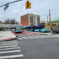 An MTA bus drives on a new red bus lane. The intersection in front of it has freshly painted crosswalks and new pedestrian ramps.