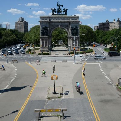 Two lanes of pedestrian and cyclist traffic go in and out of a park leading to a circle of vehicular traffic around the Soldiers' and Sailors' Arch in Grand Army Plaza.