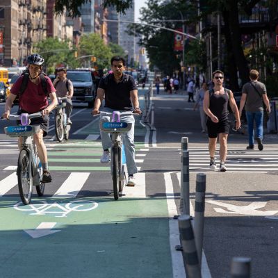 Multiple people cycle and walk along roadway space transformed into dedicated bike lanes for bicyclist and expanded sidewalk for pedestrians.