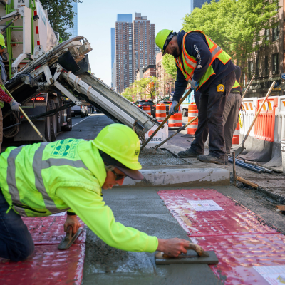 N Y C D O T employees install red pedestrian ramps along a curb.