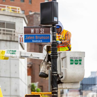 An N Y C D O T employee installs a temporary street sign named after N Y Knicks player Jalen Brunson.